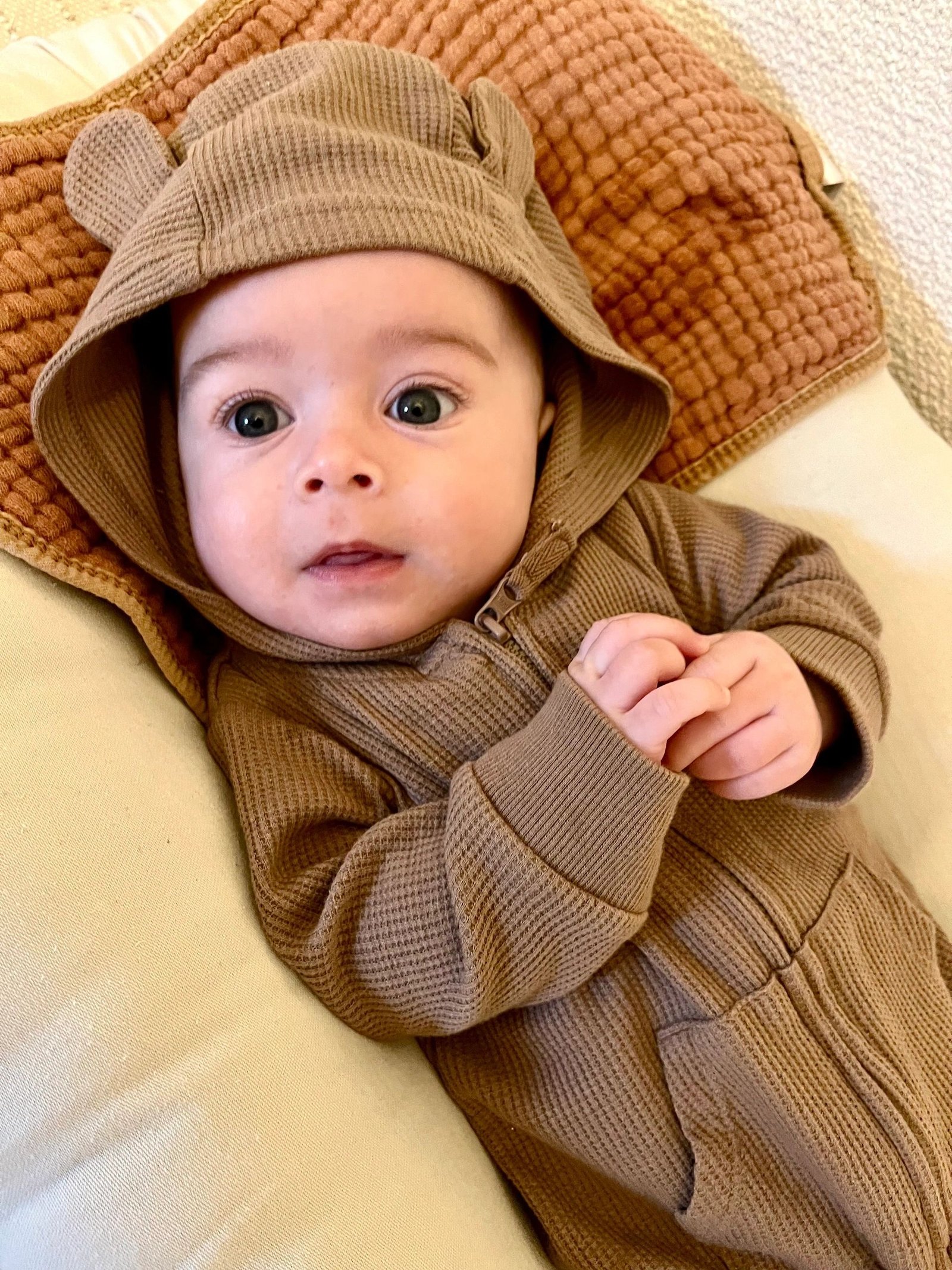 Courtland, a baby in a soft brown hooded outfit, resting on a knitted blanket