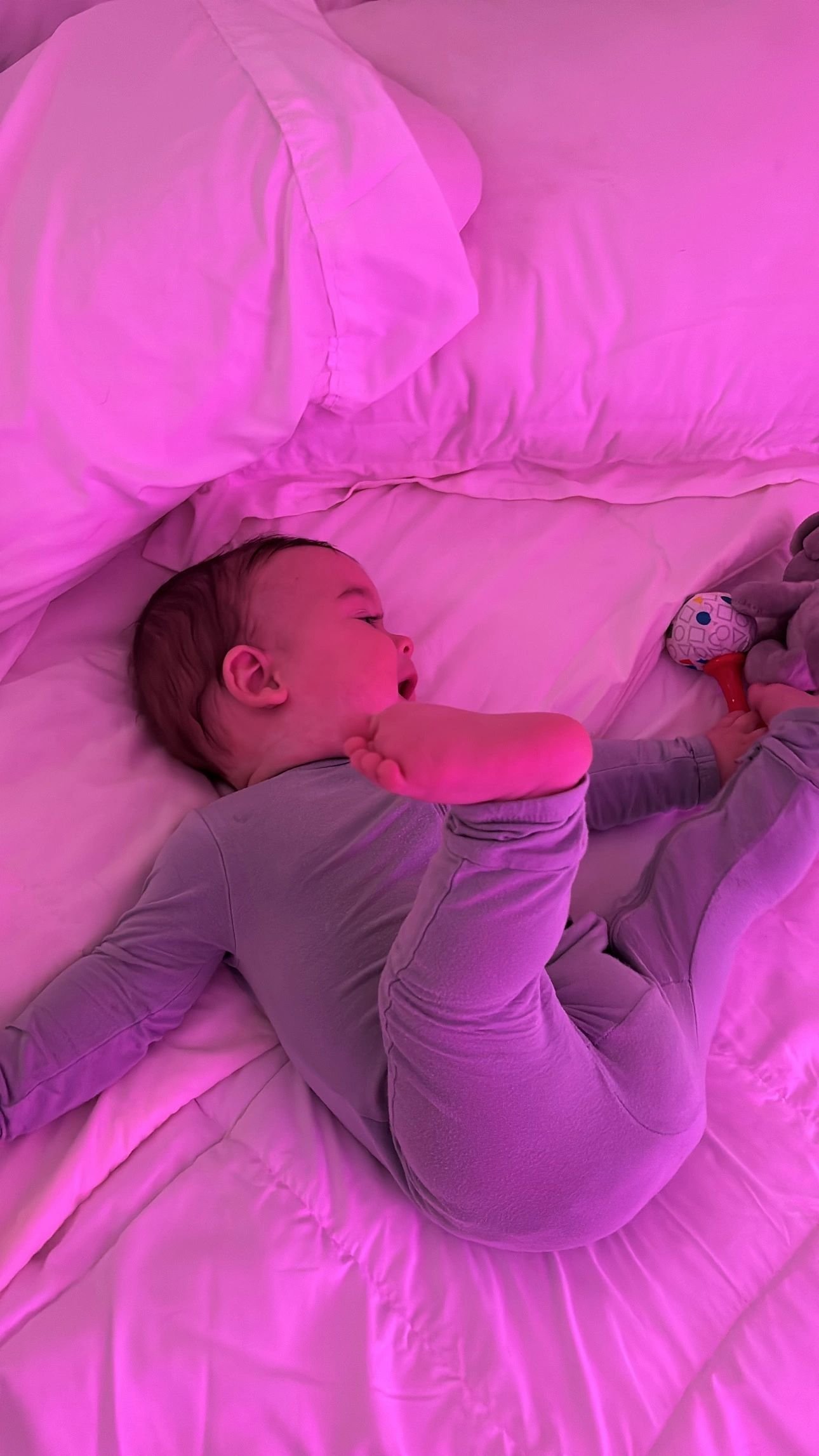 Baby in lavender pyjamas stretching on a soft bed
